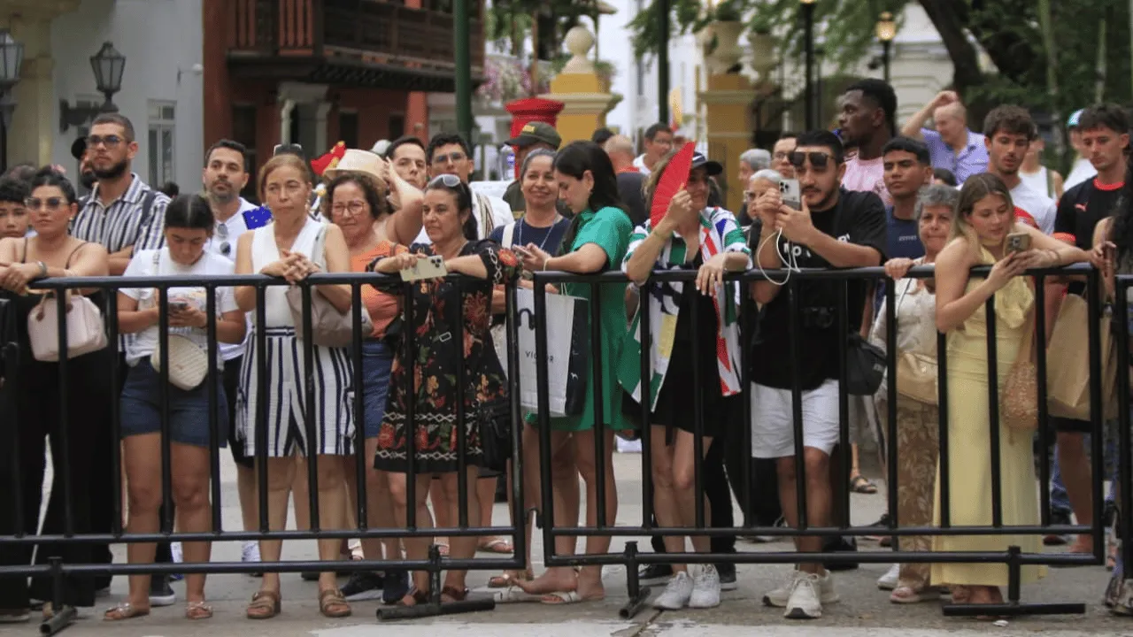 Grupo de personas detrás de vallas graba con celulares frente a casas de balcones.
